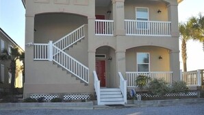 Un edificio de dos plantas con fachada color crema, una puerta roja y una escalera blanca que conduce a la entrada.
