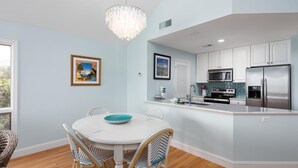 A modern kitchen with white cabinets, stainless steel appliances, and a dining area with wicker chairs and a white table.