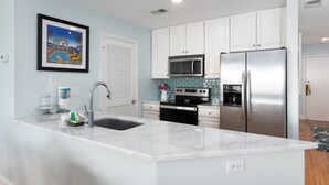 A modern kitchen with white cabinets, stainless steel appliances, a marble countertop, and a tiled backsplash.