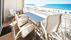 A balcony with a table and chairs overlooking a beach with umbrellas. - Gulf Dunes 413 • Amazing 5th Floor Condo, Direct Ocean View, Okaloosa Island, Free Beach Service (Fort Walton Beach)