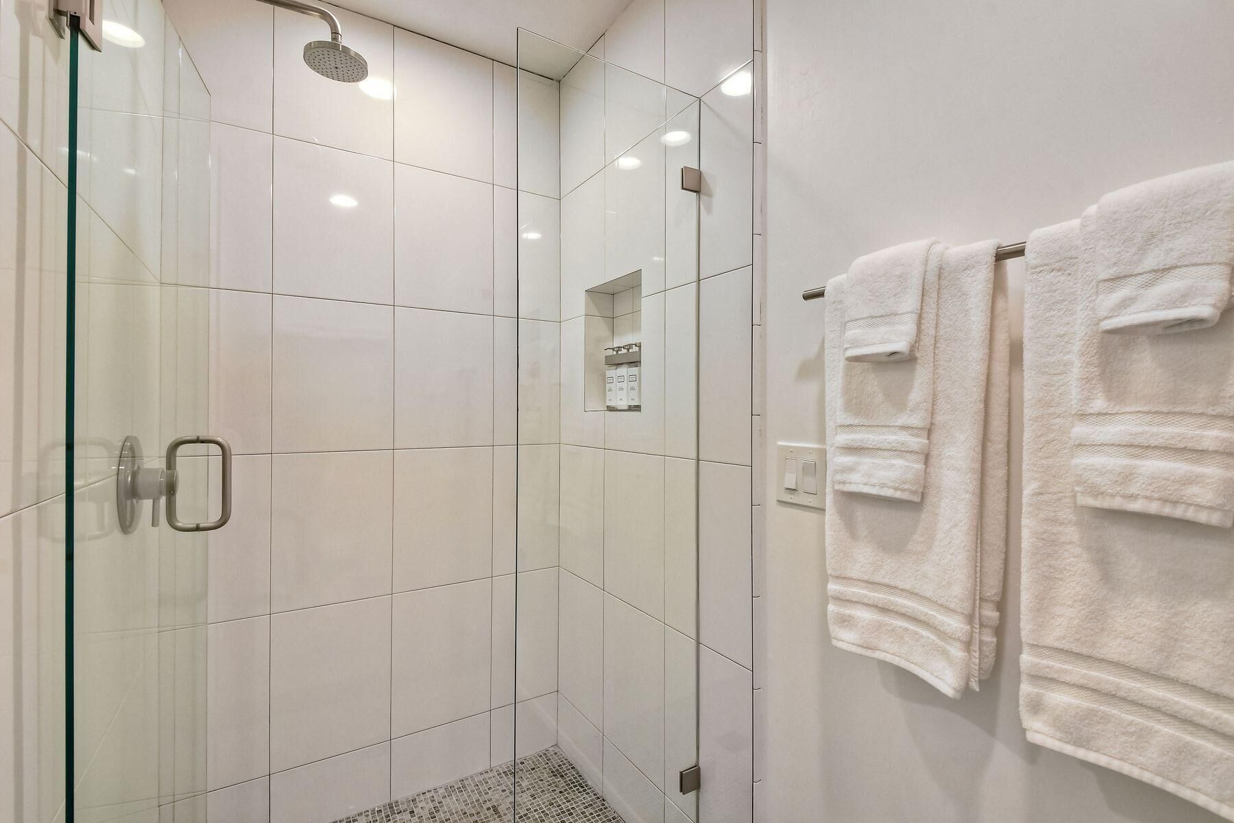 Un bagno moderno con doccia vetrata, piastrelle bianche e due asciugamani su un porta-asciugamani.