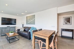 Uma sala de estar moderna com sofá, mesa de centro, mesa de jantar de madeira com cadeiras, televisão de tela plana e obras de arte nas paredes.