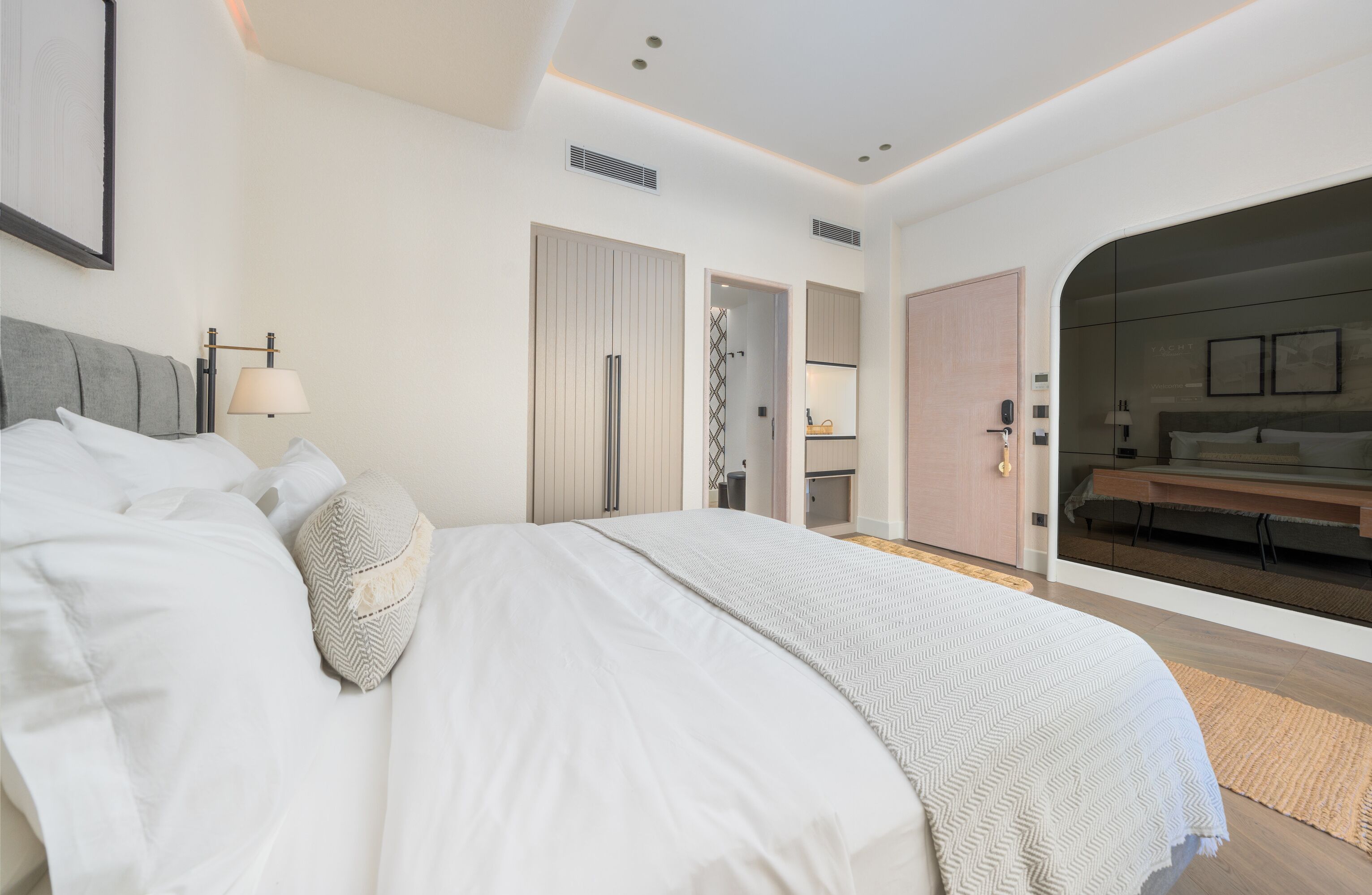 A modern hotel room with a large bed, a desk, and a bathroom visible through an open door.