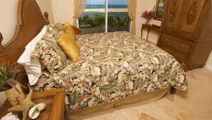 Un dormitorio con cama, cabecera de madera, mesita de noche, cómoda y vista a la playa a través de una puerta corrediza.