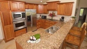 Una cocina con gabinetes de madera, electrodomésticos de acero inoxidable, encimeras de granito y una isla central con pileta.