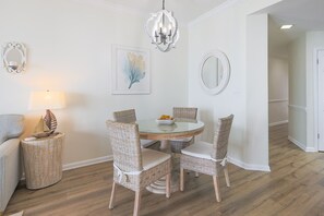 A dining area with a round table, wicker chairs, a chandelier, and a wall-mounted mirror.