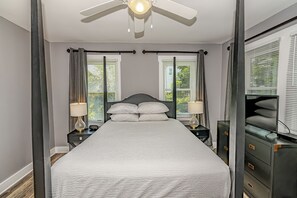 Une chambre à coucher comprenant un lit, des tables de chevet, un ventilateur de plafond et une commode.