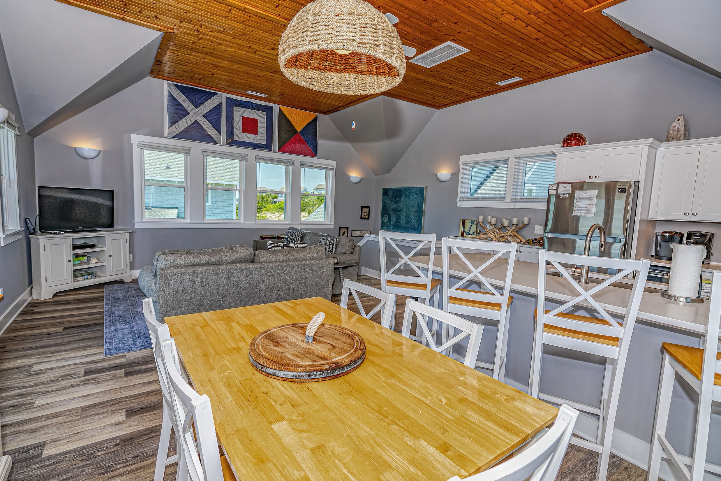 Une cuisine moderne avec des meubles blancs, un réfrigérateur en acier inoxydable et un coin repas comprenant une table en bois et des chaises blanches.