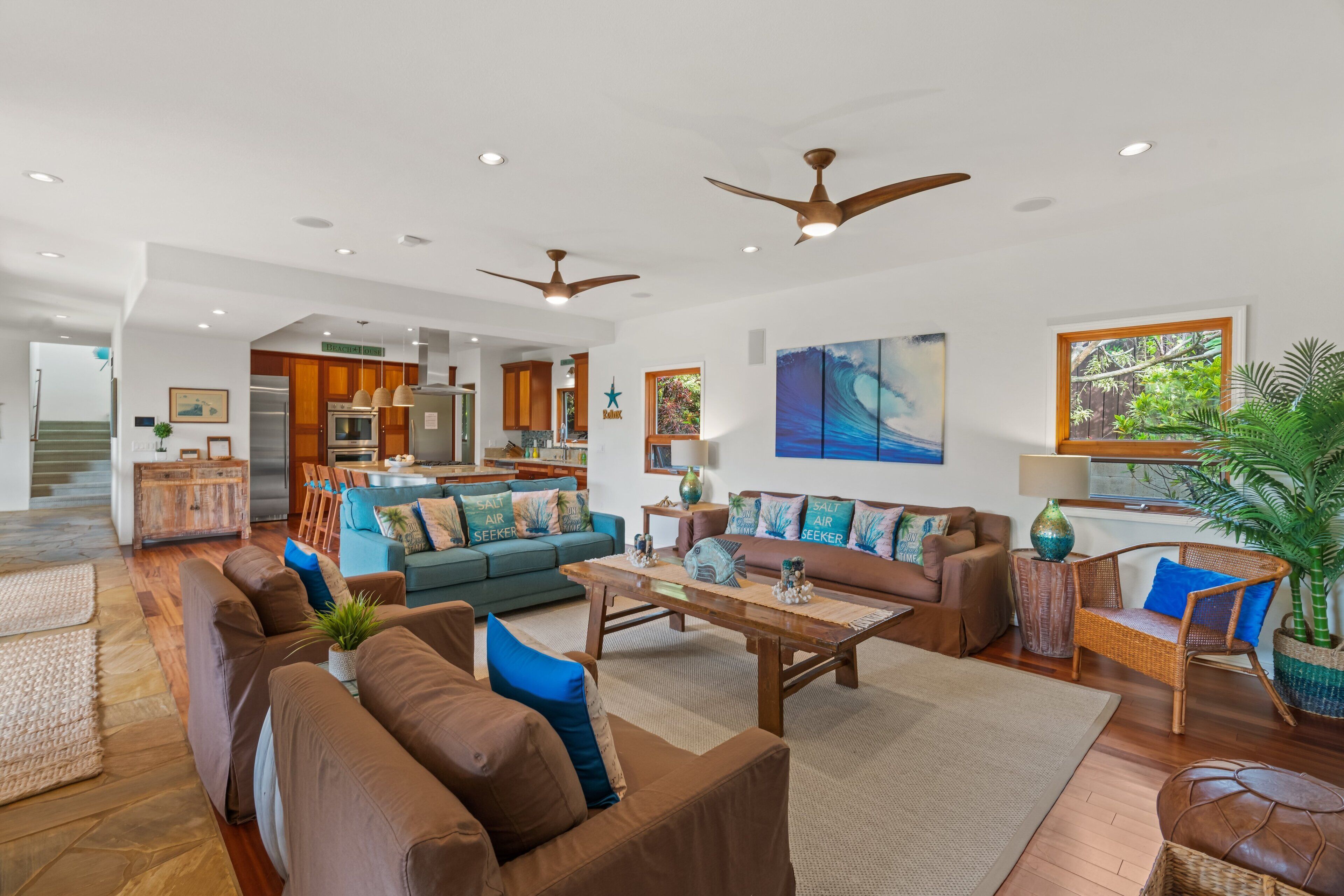 A spacious living area with a large sofa set, a coffee table, and a dining area with wooden cabinets and a kitchen in the background.