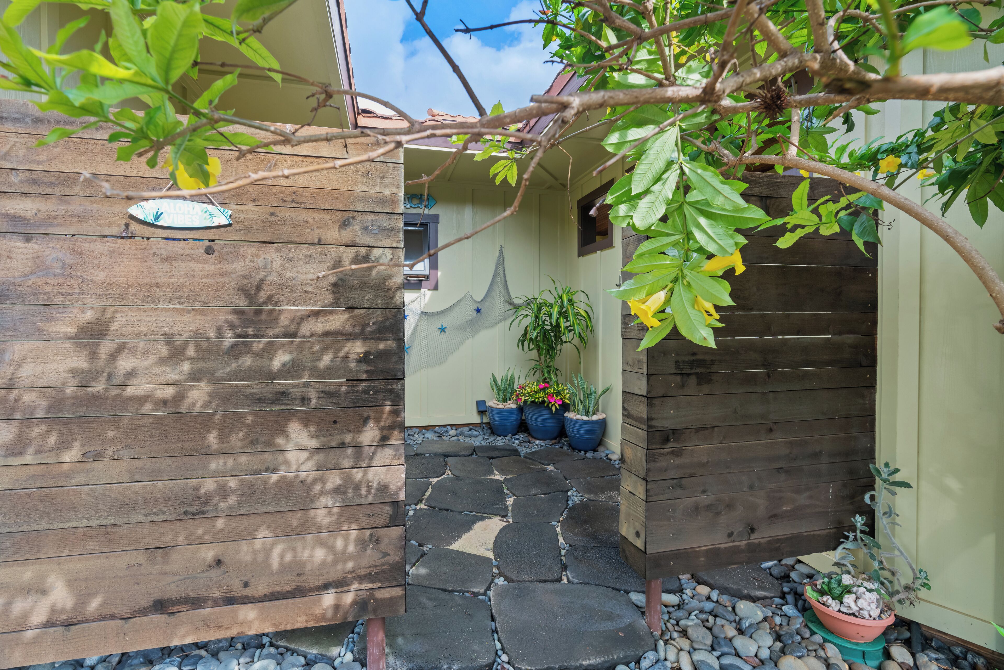 A wooden exterior with a stone pathway leading to a door, surrounded by potted plants and a small garden area.