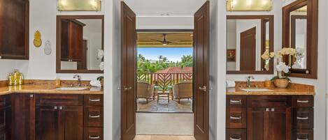 A spacious bathroom with two sinks, dark wooden cabinets, and a view of a tropical outdoor area through an open doorway.