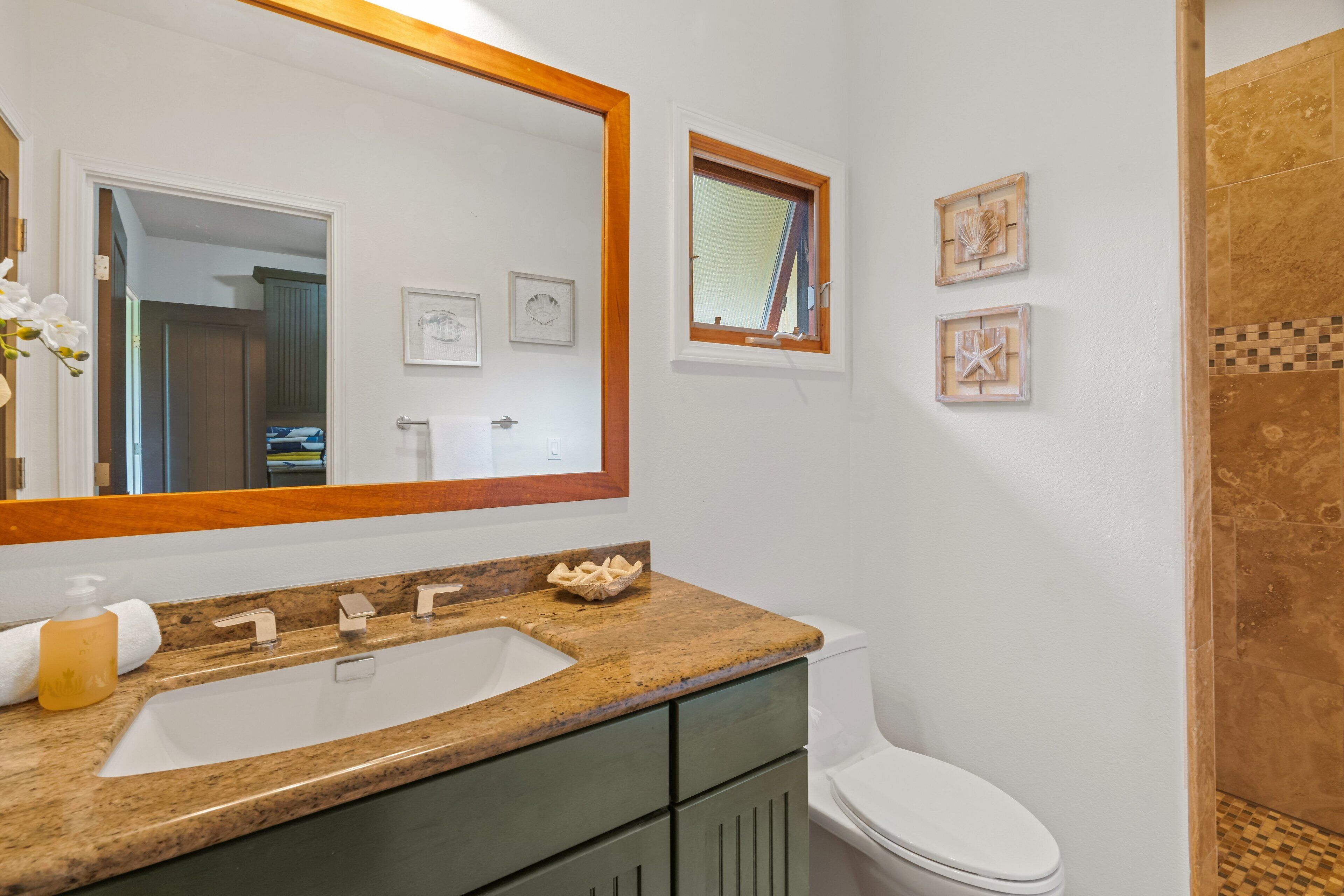 Un baño con lavamanos de encimera de granito, inodoro blanco y zona de ducha con azulejos marrones.