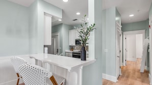 A modern kitchen with white cabinetry, a central island, and a bar stool. - Find The Best Seat at The Front Row / Quiet Area on St. Augustine Green in Rosemary / 4 Bikes (Panama City Beach)