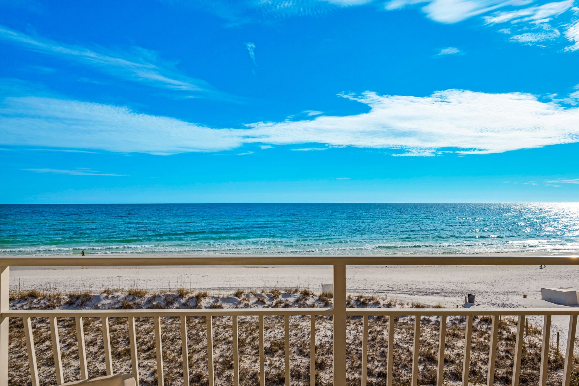 A beach view from a balcony with a railing, sandy beach, and ocean.