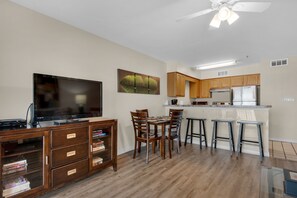 Una cocina moderna con armarios de madera, un refrigerador de acero inoxidable y una zona de comedor con taburetes de bar.