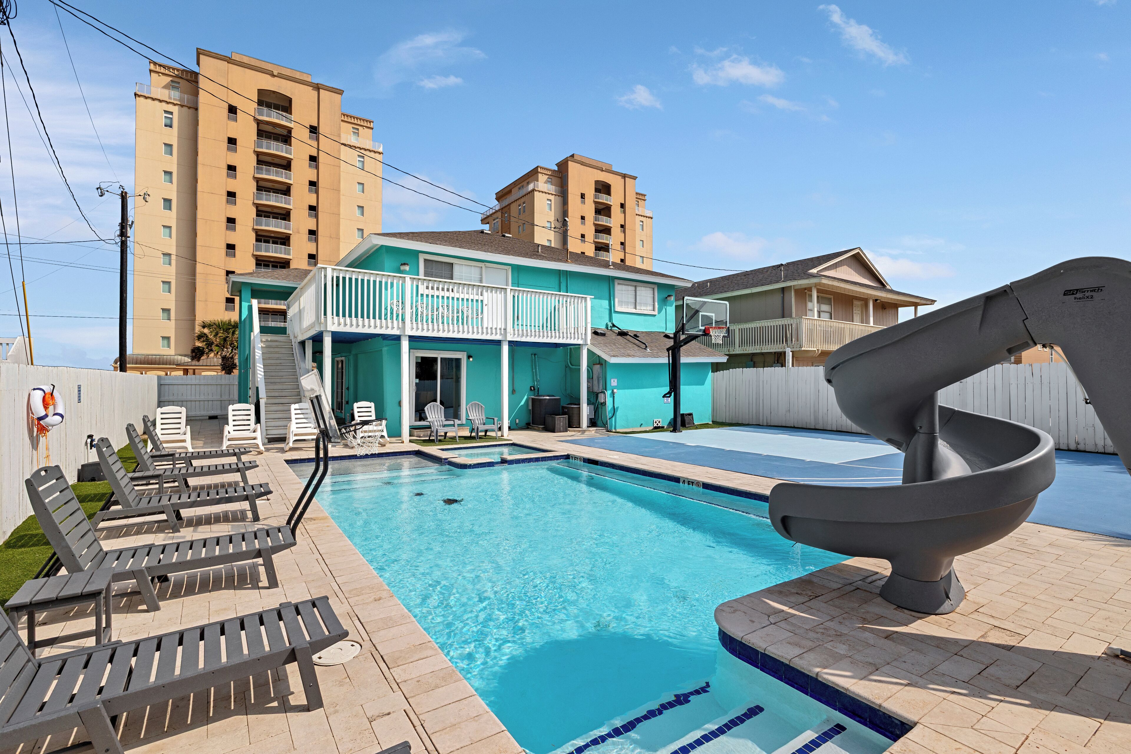 A swimming pool with lounge chairs, a slide, and a building in the background.