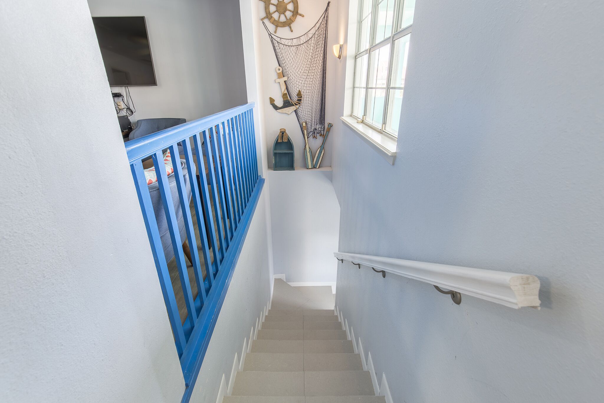 Una escalera con barandillas azules, pasamanos blancos y decoraciones náuticas, incluyendo un timón y un ancla.