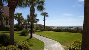 A paved pathway leading to a gazebo, surrounded by palm trees and a well-maintained lawn. - Waters Edge 109 ~ Ground Floor and Beach Front ~ Steps to Pool and Sand! (Fort Walton Beach)
