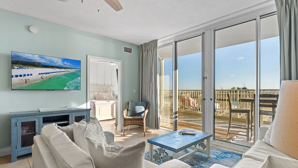 A spacious living room with a large flat-screen TV, a sofa, a chair, and a coffee table. - Waters Edge 109 ~ Ground Floor and Beach Front ~ Steps to Pool and Sand! (Fort Walton Beach)