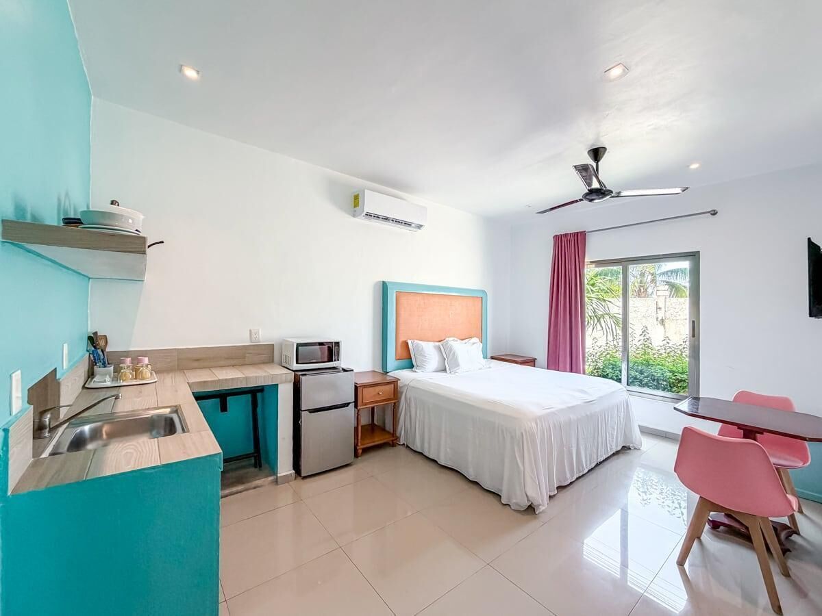 A hotel room with a kitchenette, a bed, a desk, and a view of greenery.