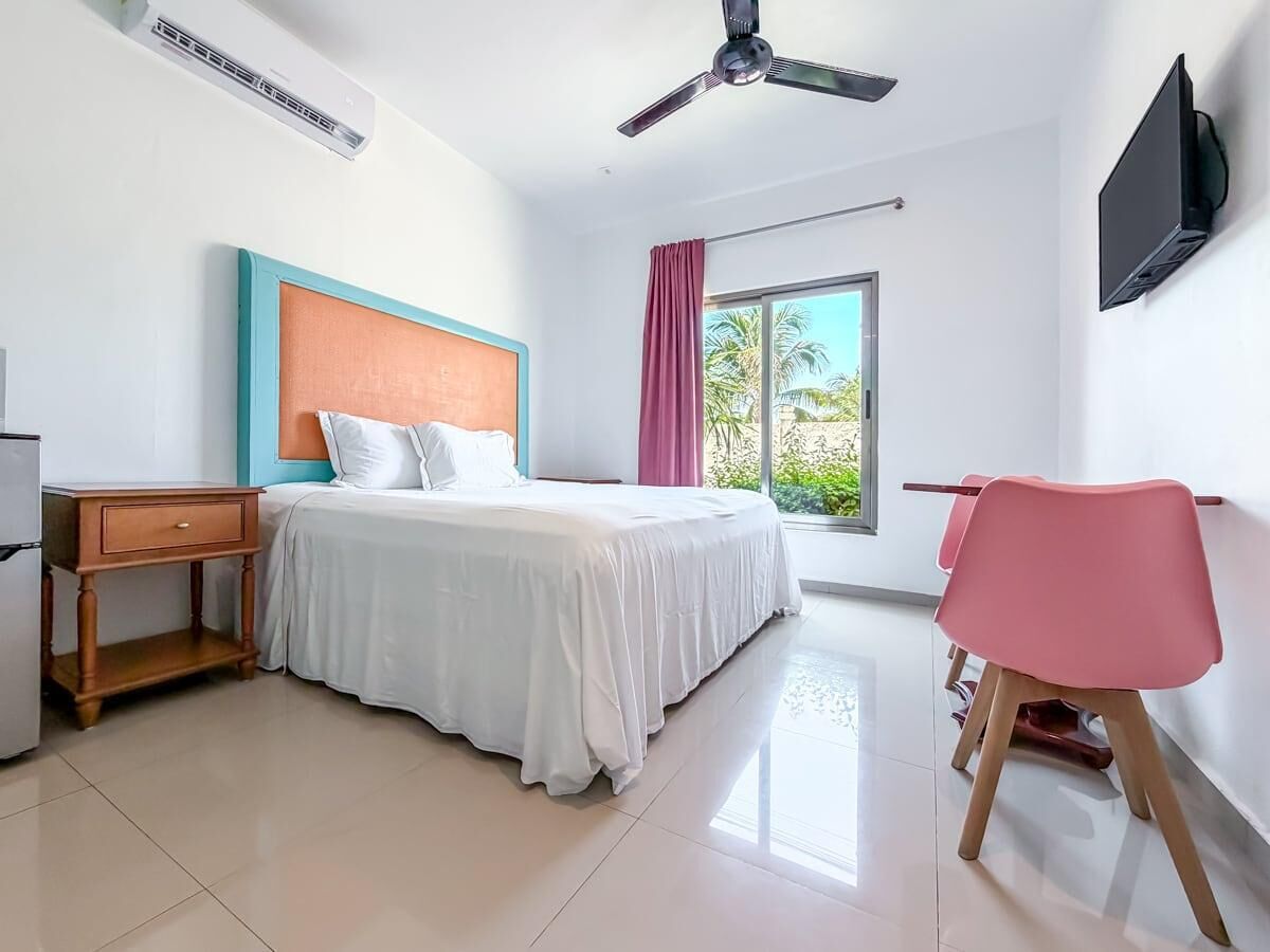 A hotel room with a bed, a desk, a chair, a TV, and a window with a view of palm trees.