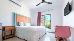 A hotel room with a bed, a desk, a chair, a TV, and a window with a view of palm trees. - Beautiful studio just steps from Downtown (Isla Mujeres)