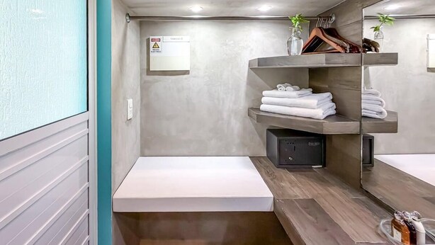 A compact bathroom with a shower, a sink, and a mirror. There are towels stacked on a shelf, and a small plant on the counter. - Beautiful studio just steps from Downtown (Isla Mujeres)