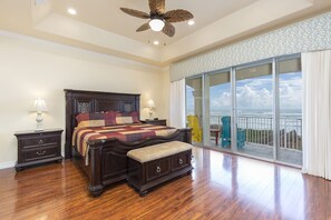A spacious bedroom with a large bed, wooden floor, and a balcony with a view of the ocean.