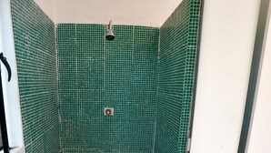 Ett litet badrum med ett vitt handfat på en piedestal, gröna kakelväggar och en duschhörna.