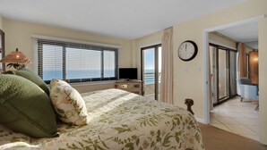 Ein Schlafzimmer mit Bett, Fernseher, einer Uhr und Meerblick durch ein Fenster.