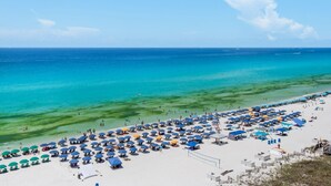 Ein Strand mit vielen Sonnenschirmen und Liegestühlen, einem klaren blauen Meer und einem sandigen Ufer.