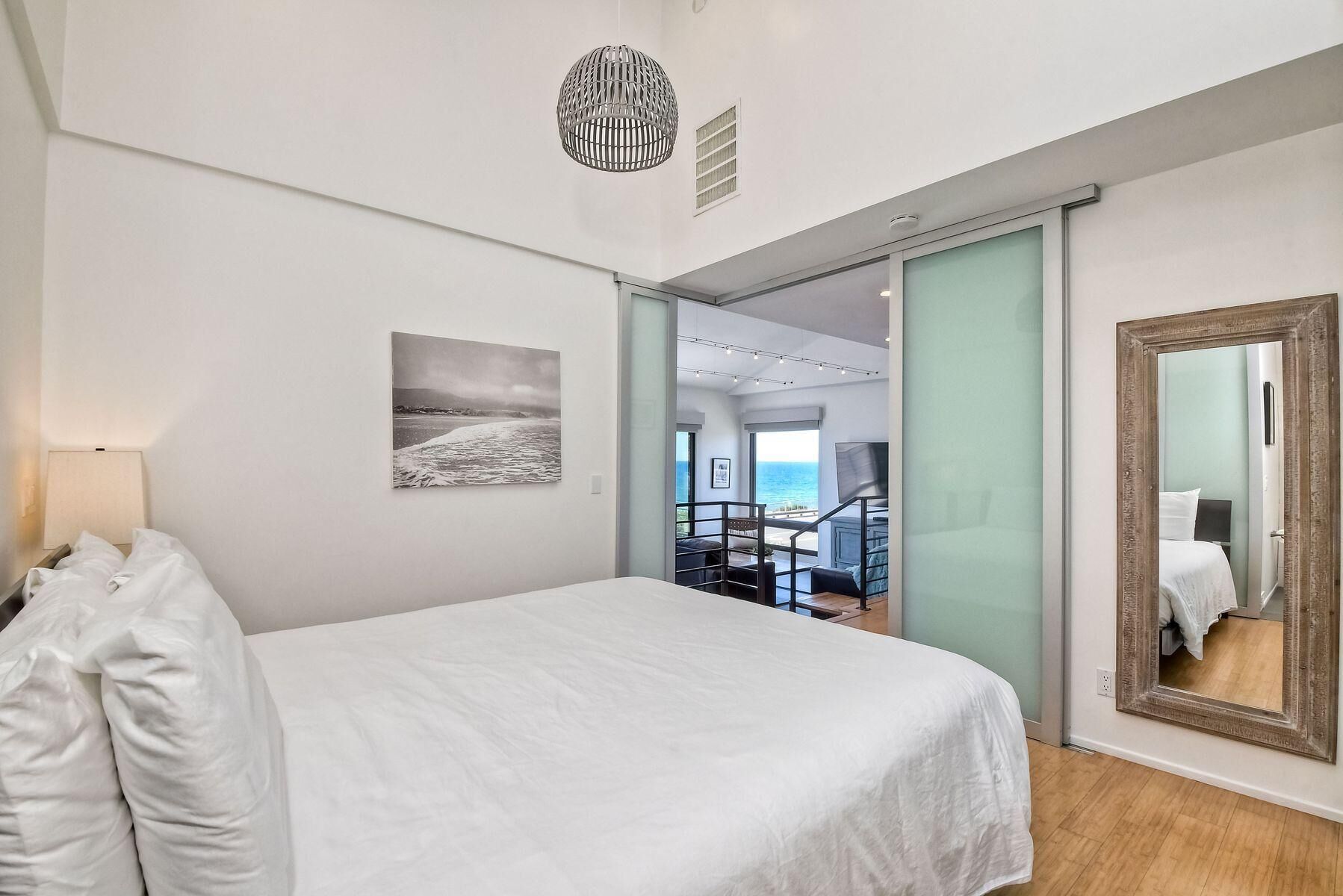 Une chambre à coucher avec un lit, un grand miroir et une vue sur la mer, visible à travers une porte vitrée.