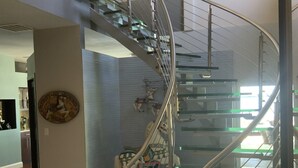 Una escalera en espiral moderna con escalones de vidrio y barandillas metálicas, que conduce a un piso superior.