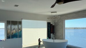 Un dormitorio moderno con un ventanal grande, un ventilador de techo y una bañera.