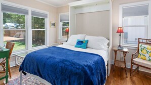 Un dormitorio con cama, una silla, una mesa y una ventana.