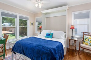 Een slaapkamer met een bed, een stoel, een tafel en een raam.