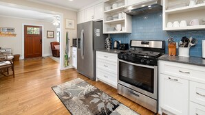 A modern kitchen with white cabinets, stainless steel appliances, and blue backsplash tiles. - Dog Friendly | Huge Privacy Fenced Backyard | Close to Village and Beaches (St. Simons Island)