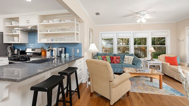 Una cocina moderna con una isla central, taburetes de bar y una zona de comedor con un sofá azul y una mesa de centro.