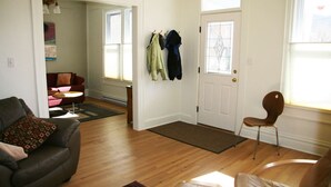 A living room with a dark brown leather sofa, a brown leather armchair, and a wooden floor. There is a door with a glass panel and a coat rack with jackets hanging on it. - Comfort by the river & short walk to downtown. (Salida)