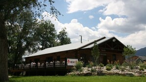 A rustic log cabin with a balcony, surrounded by greenery and mountains in the background. - Comfort by the river & short walk to downtown. (Salida)