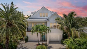 A two-story house with a garage, surrounded by palm trees and a driveway.