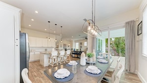 A modern kitchen with a central island, pendant lighting, and a dining area with chairs and a table set for a meal.