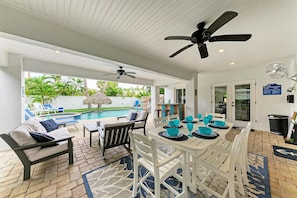 Área externa coberta com piscina, mesa de jantar, cadeiras, ventiladores de teto e vista para a piscina.