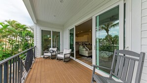 A covered deck with outdoor furniture, a sliding glass door leading to a living area, and a view of palm trees.