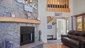A stone fireplace, a brown leather sofa, and a wooden bench in a living room with a stone wall and a view of the outdoors. - Beside Quiet Waters | Waterfront | Lake Bellaire (Bellaire)