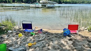 A lakeside view with boats, a sandy area with beach chairs, and a flag. - Beside Quiet Waters | Waterfront | Lake Bellaire (Bellaire)