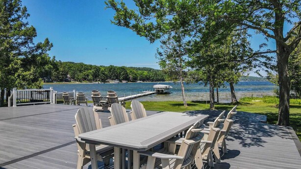 A deck with a table and chairs overlooking a lake, surrounded by trees and a dock. - Beside Quiet Waters | Waterfront | Lake Bellaire (Bellaire)