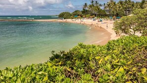 A beach with clear turquoise water, palm trees, and beach umbrellas. - Keone Nani Condo - New AC, Golf, Swim, Food Trucks (Kahuku)