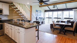A spacious kitchen with a central island, a dining area with a table and chairs, and a staircase leading to an upper level. - Keone Nani Condo - New AC, Golf, Swim, Food Trucks (Kahuku)