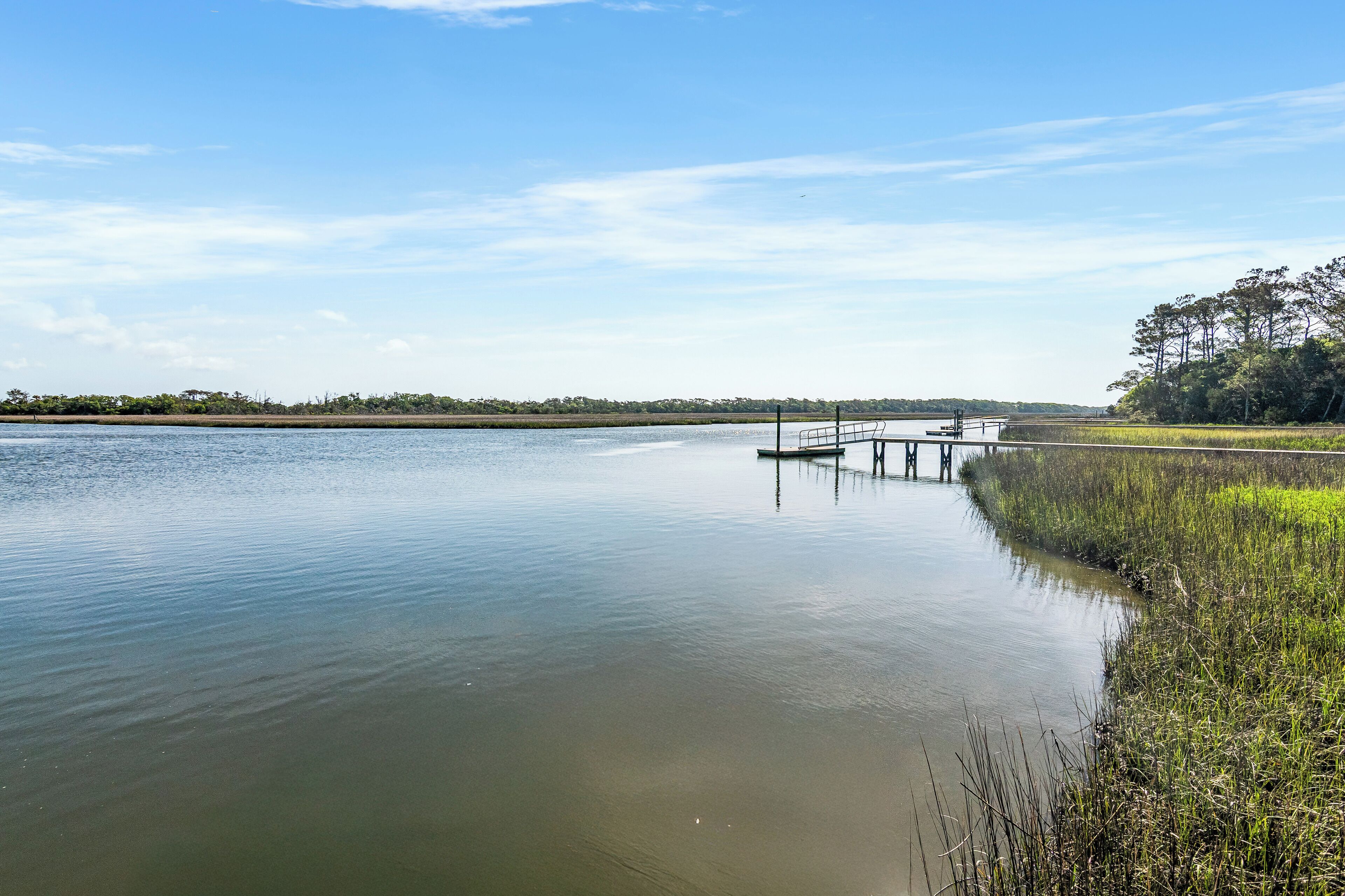 A calm lake with a dock extending into the water, surrounded by grassy areas and trees.
